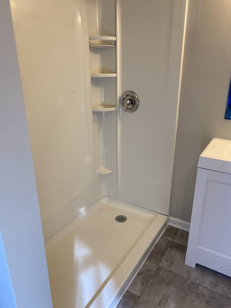 Finished corner shower with a moulded pan, built-in corner shelves and a fixed showerhead.