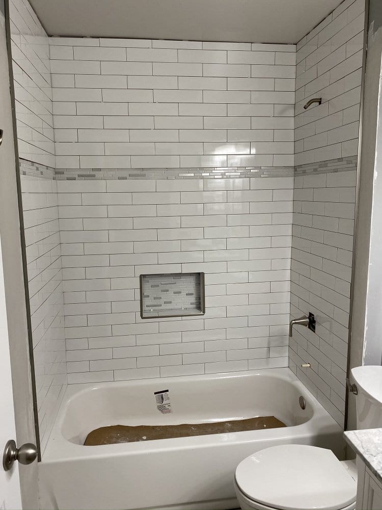 Finished tub and shower in white subway tile with a mosaic accent band and a recessed shampoo niche.