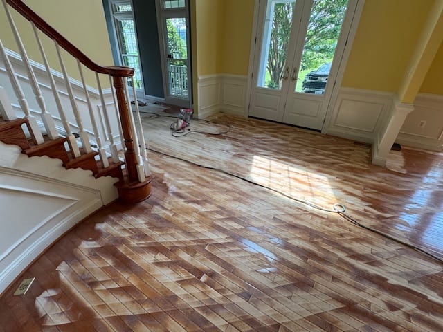 Living room with a newly refinished hardwood floor beside a staircase and tall windows.
