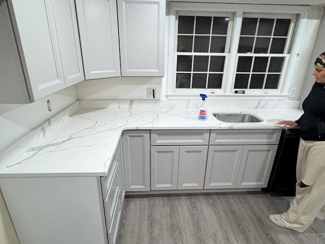 Finished white kitchen cabinet run with a marble-look counter and sink below a wide window.