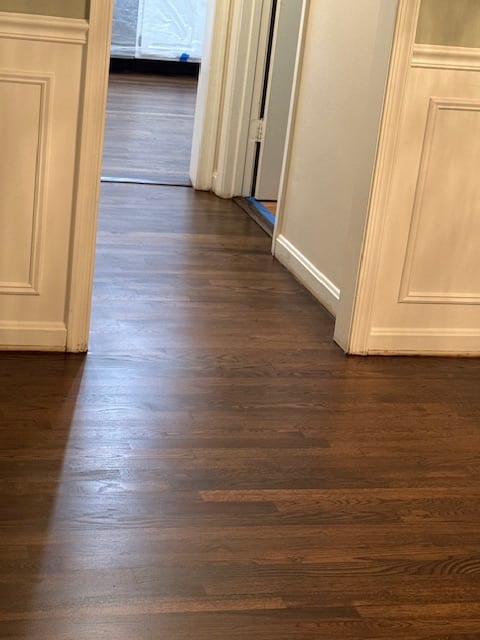 Finished dark hardwood floor running along a white kitchen cabinet base.