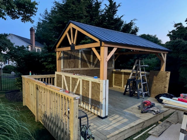 Timber covered-deck structure under construction with gable framing and new railings.