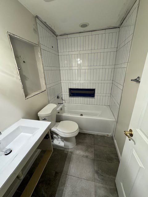 Finished bathroom with white tub, large grey shower tile and a white vanity.