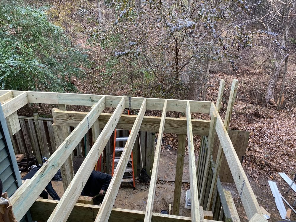 New pressure-treated deck framing built out over a sloping wooded yard, posts and beams in place before boards go down.