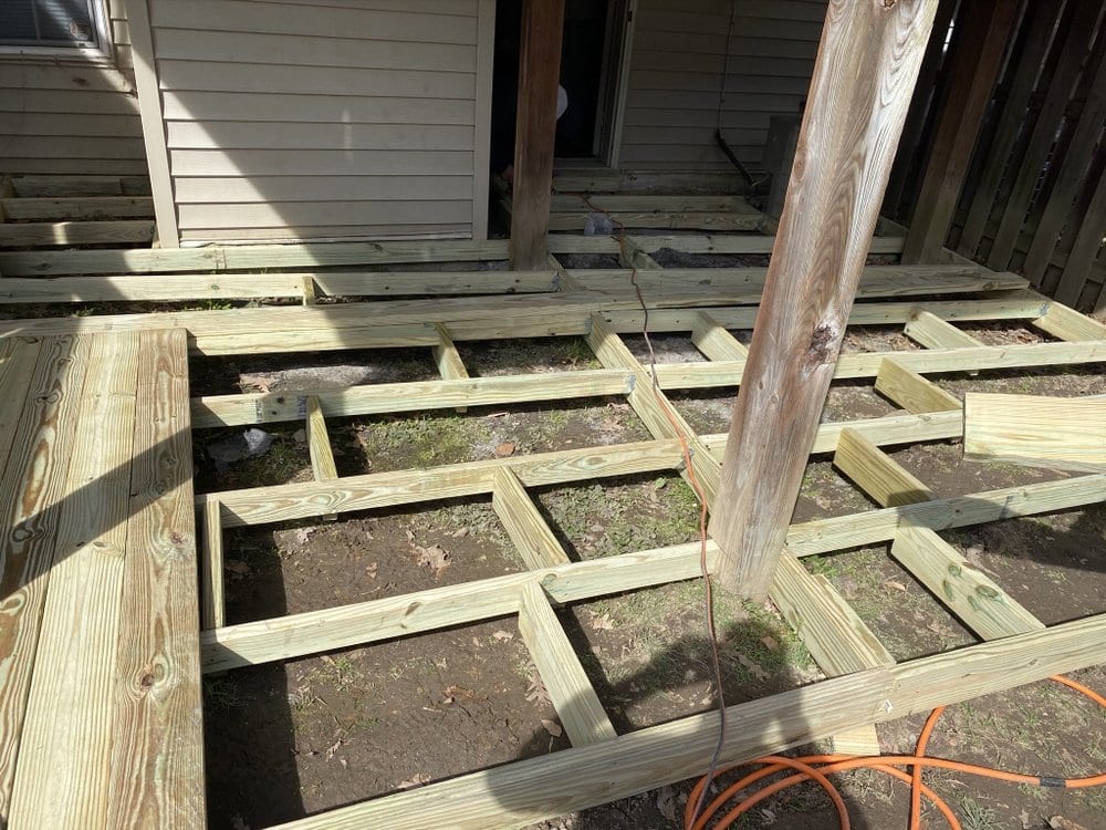 Close view of pressure-treated deck joists framed tight around a standing post, seen from above before decking is laid.