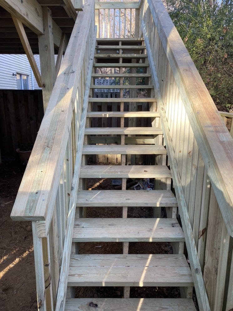 Wooden deck stairs under construction, stringers set between framing with treads partly installed.