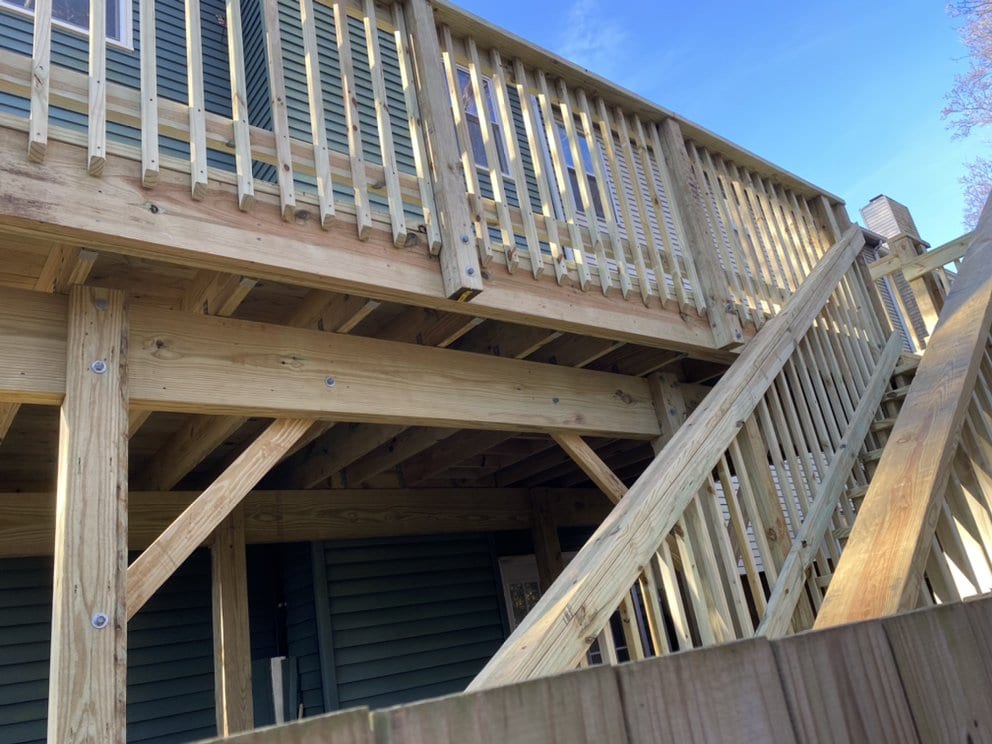 View beneath a completed deck showing support posts, a built-up beam and stair stringers.