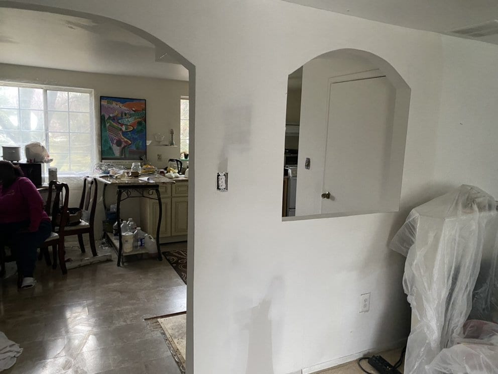 Interior wall with a newly framed and boarded arched pass-through, taped and ready for finishing, furniture sheeted off.