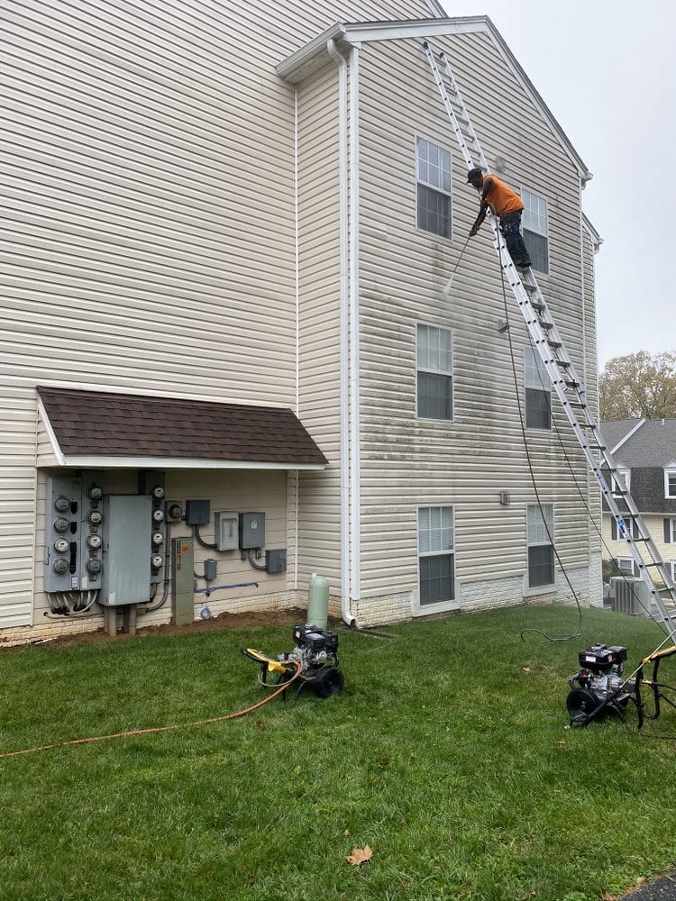 A worker in high-visibility clothing up an extension ladder against the upper siding of a three-storey house.