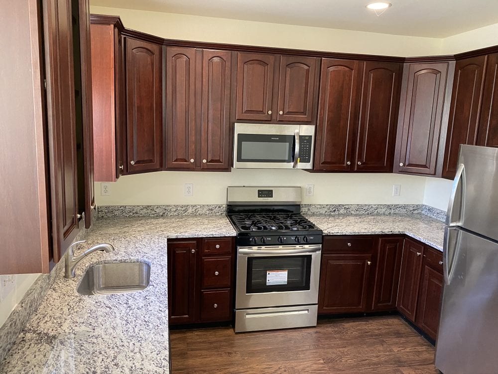 Finished kitchen with raised-panel cherry cabinets, light granite counters, stainless range and refrigerator.