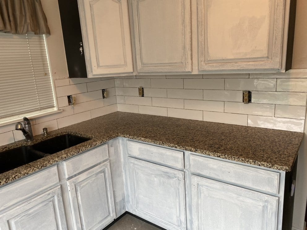 Finished kitchen corner with pale cabinets, granite counter and white tiled backsplash.