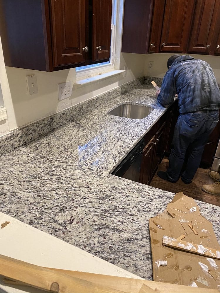 A worker fitting a speckled granite countertop onto dark base cabinets during a kitchen installation.