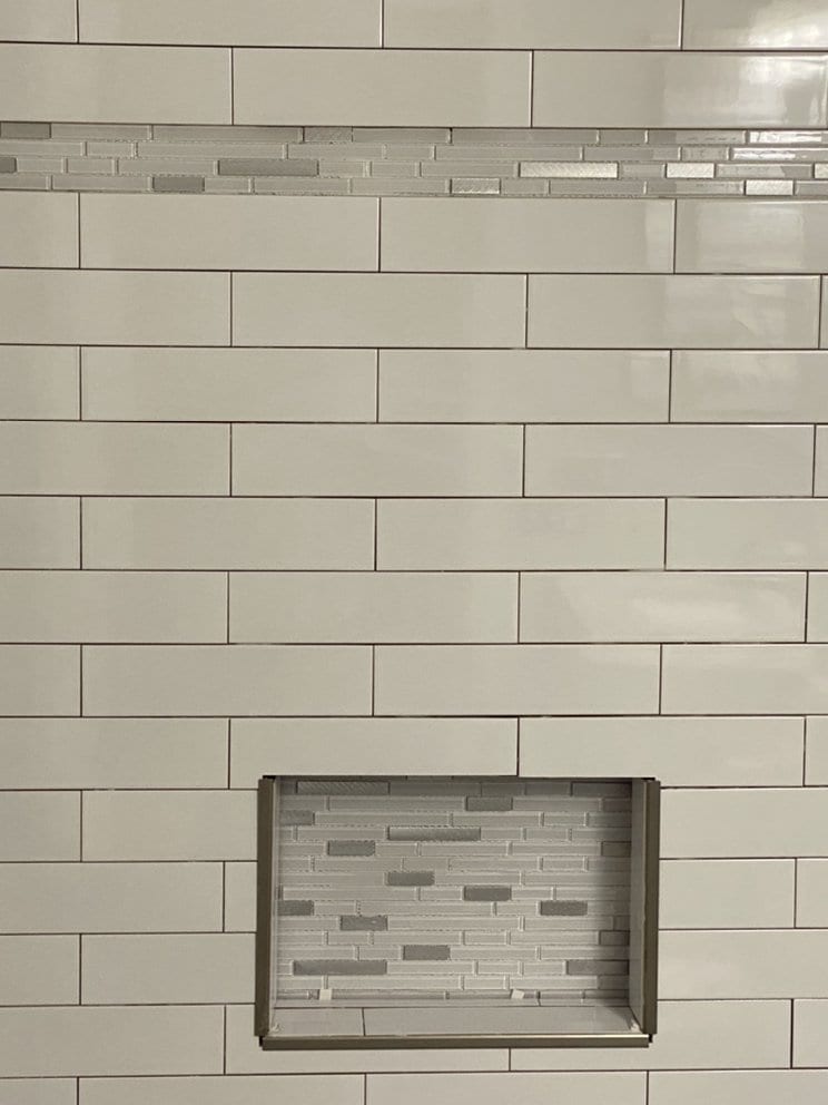 Close view of a recessed shower niche lined in mosaic tile, set into a wall of white subway tile.