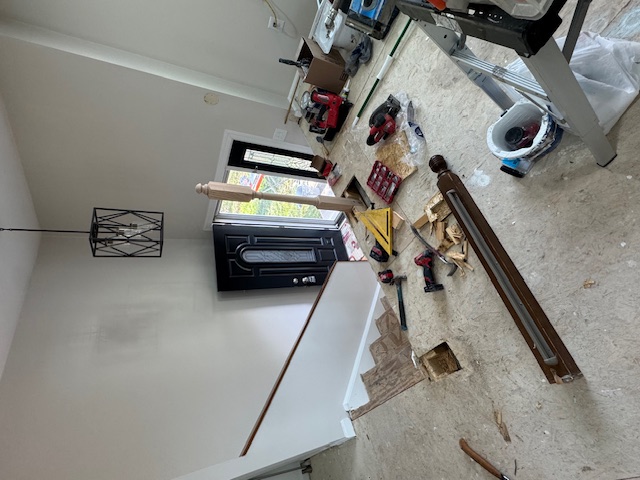 Split-level interior with tools and new railing components laid out beside the stairs.