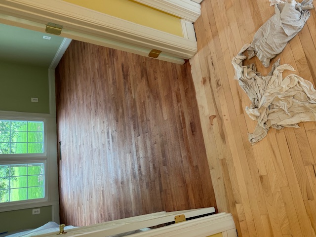 Room showing a hardwood floor partly stripped and partly stained during refinishing.