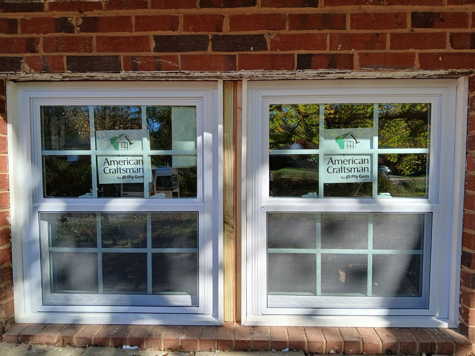 Two finished white replacement windows installed in a red brick exterior wall.
