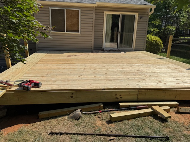 Pressure-treated deck with the surface partly boarded and tools set near the unfinished edge.