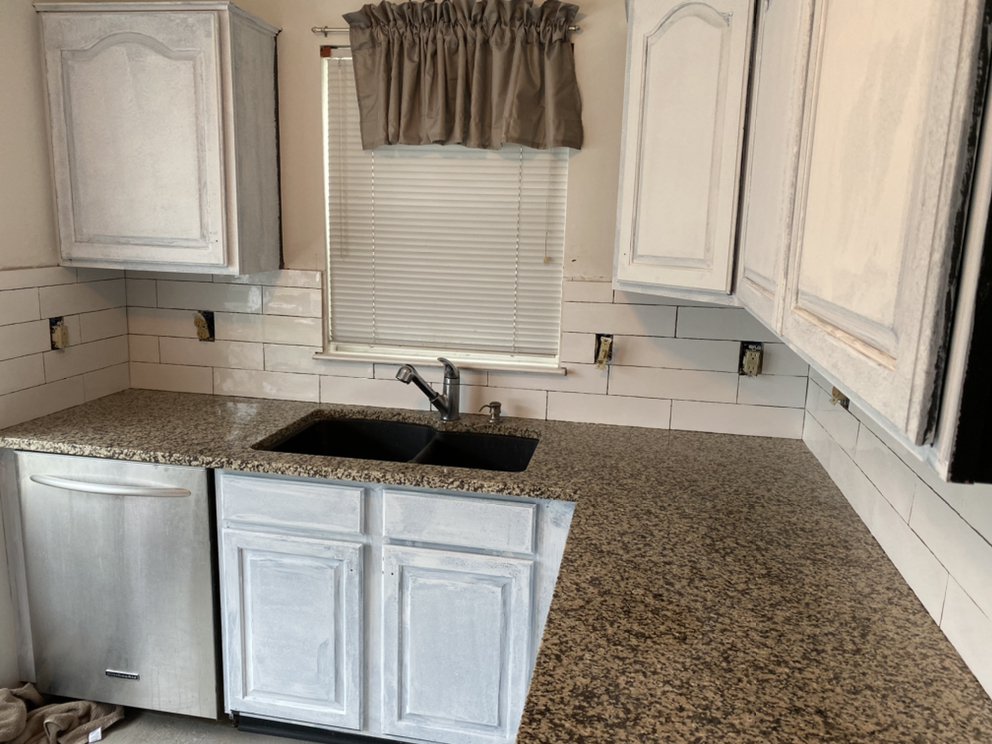 Finished kitchen with a double bowl sink under a curtained window, granite counters and pale cabinets.
