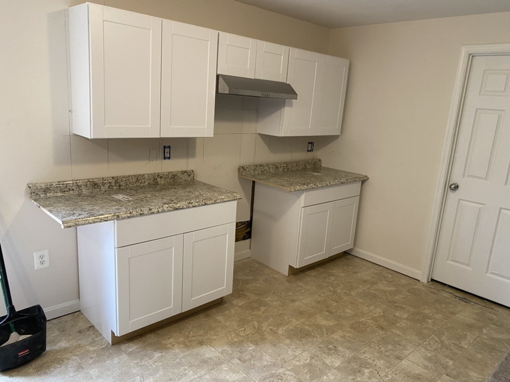 Newly installed white wall and base cabinets with granite tops in an otherwise empty kitchen.
